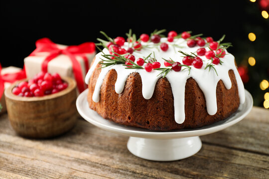 Delicious Christmas cake with icing, cranberries and rosemary on wooden table against black background with blurred lights, closeup with space for text. Bokeh effect