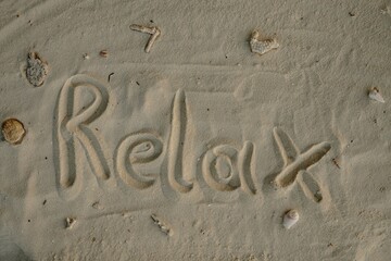 Word RELAX Written in Sand with Shells and Coral Pieces