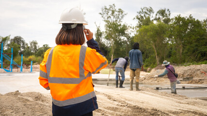 A supervisor in safety gear watches over workers on a construction site. Several individuals are engaged in various tasks, ensuring the project moves forward smoothly