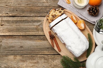 Traditional Christmas Stollen with icing sugar, spices, tangerine and festive decor on wooden table, flat lay. Space for text