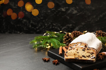 Traditional Christmas Stollen with icing sugar, spices and festive decor on black table, space for text. Bokeh effect
