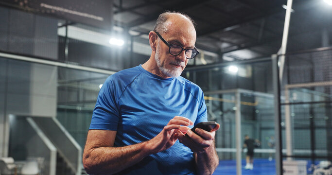 Padel, senior man and texting with phone on court for match update, track performance or game break. Retirement fitness, old person and smartphone at indoor tennis club for practice schedule and chat - Powered by Adobe