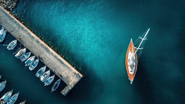 Aerial view of a marina with a wooden sailboat anchored in clear blue water. Several smaller boats line a dock to the left, creating a serene scene generative ai - Powered by Adobe