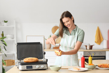 Young woman cooking hot dog with fried onion in kitchen