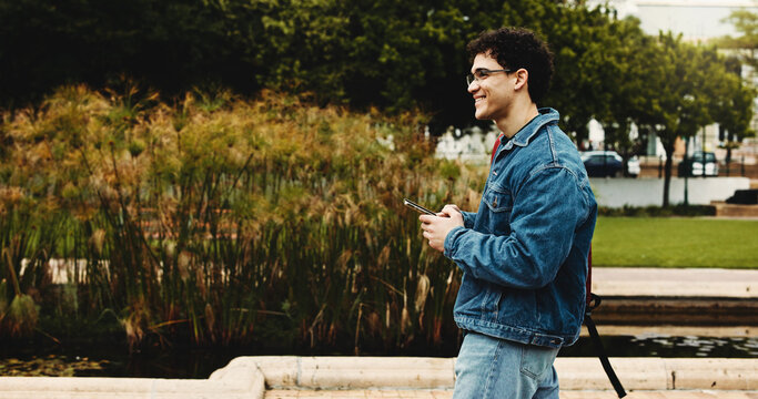 College, walking and man with phone for social media, thinking and online message on campus. University, academy and student on smartphone for networking, internet and thoughtful on journey to class