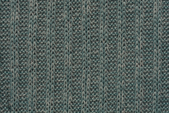 A detailed, full-frame close-up of a tightly woven, geometric rib knit fabric in a muted blue-gray color, creating a repetitive diamond-like texture