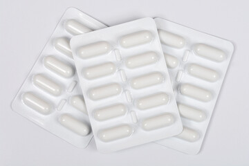 An overhead view of three white blister packs containing white oval capsules, overlapping...
