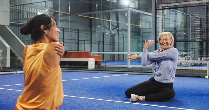 Women, coach and stretching arms at padel club, smile and advice for training, routine and talk. Personal trainer, senior person and happy with warm up, fitness and chat with exercise on tennis court - Powered by Adobe
