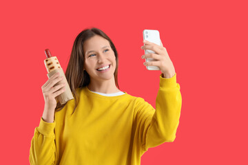 Young woman with tasty hot dog taking selfie on red background