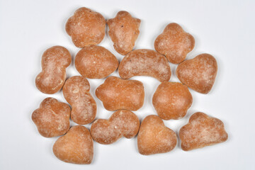 An overhead view of a scattered pile of small, unglazed gingerbread cookies cut into various shapes, including hearts, on a white background