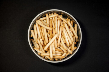 Small breadsticks on white plate on black background