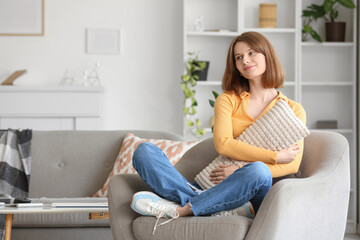 Fototapeta premium Young woman with pillow sitting in grey armchair at home