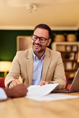 Professional Man In Beige Blazer Meets Client For Paperwork, Laptop Review, And Friendly Discussion