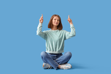 Young woman pointing at something on blue background