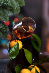 Brandy in a glass and tangerines. Dark background. A festive drink. Spruce branches in the background. The New Year holiday.