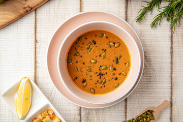 Warm lentil soup served with pumpkin seeds, lemon slice and crispy croutons on wooden table