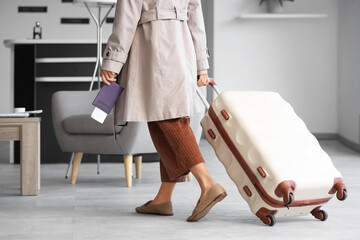 Young woman with passport and suitcase walking in airport lounge, back view