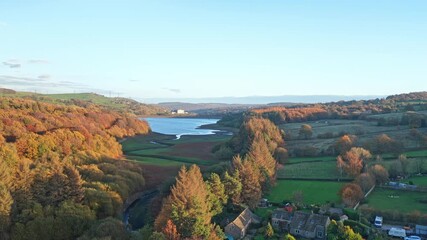 Rising aerial ascent reveals Underbank Reservoir's expanse nestled within dense woodlands and moorland valleys, with Stocksbridge village and the northern Peak District countryside in autumnal colors.