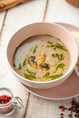 Bowl of creamy mushroom soup with herbs and oil served with crispy croutons on pink plate