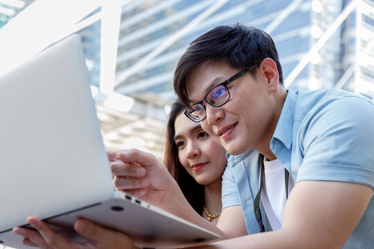 Happy young asian couple celebrates investment success with profits stock market, gold and bitcoin cryptocurrency trading. man and woman checking financial portfolio on laptop, ai finance planning.