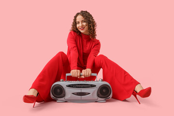 Beautiful young woman with boombox sitting on pink background