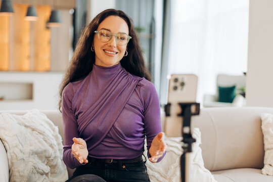 Cheerful smiling woman blogger wearing stylish eyeglasses talking recording video using mobile phone