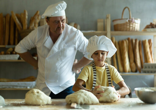 Little daughter and father make dough together in bakery kitchen