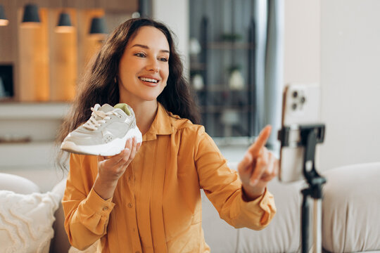 Smiling middle aged woman showing shoes, blogger recording video sitting in modern living room