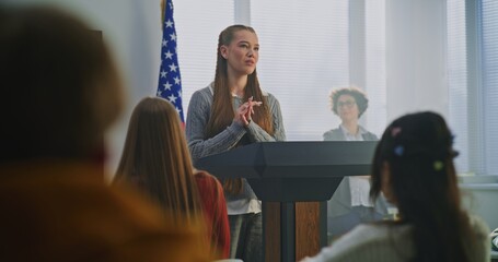 American Teenage Girl Delivers Expressive Speech in Front of Classmates, Gesturing Confidently With US Flag. Concept Civic Education, Confident Communication, Active Student Participation. Dolly Shot.