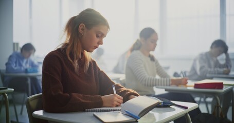 Teenagers Writing Completing Task in Classroom. Diverse Group of Students Sits Desks in Focusing Intently on Writing Assignments. Concept Student Concentration, Academic Workload in Modern Education.