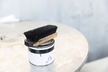 Shoe polish tin and black wooden brush sitting on a metallic surface, ready for leather care.