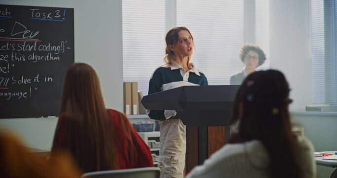 Beautiful Teenage Girl Stands Podium, Delivering Report Classmates in Bright, Modern Classroom. Concept of Student Engagement, Confidence Building, and Communication Skills Development. Dolly Shot.