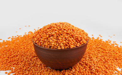 Clay cup with red lentils and lentils scattered around on white background.