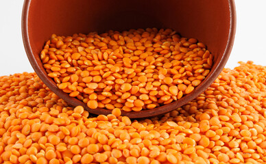 Red lentil background. Beautiful red lentils spill out of a clay cup.