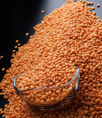 Red lentils spilling out of a glass cup on a black background. Close-up.