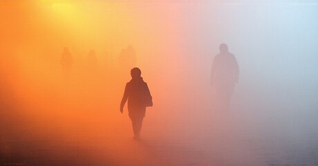 Fototapeta premium Silhouettes walk toward viewer. Orange, pink hues dominate foggy landscape. Mysterious, ethereal mood pervades scene.