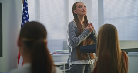 American Teenage Girl Delivers Expressive Speech in Front of Classmates, Gesturing Confidently With US Flag. Concept Civic Education, Confident Communication, Active Student Participation. Dolly Shot.