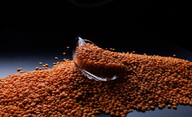 Red lentil background. Glass cup on a pile of red lentils on a black background.