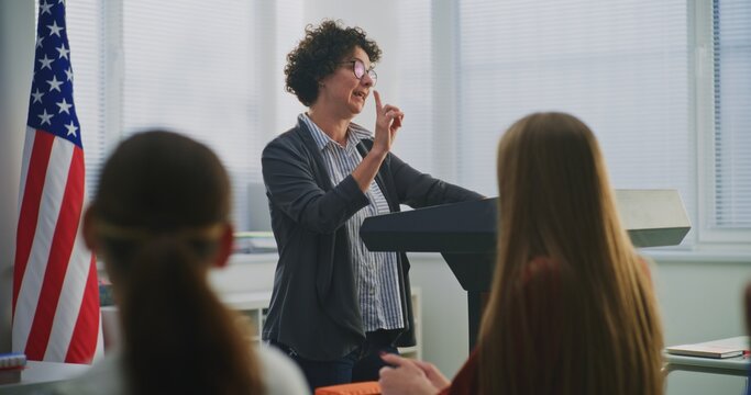 American Teacher Stands Podium Beside US Flag, Engaging Students In Open Discussion About National Values, Civic Responsibility. Concept Patriotic Education, Identity, Positive Learning Environment.