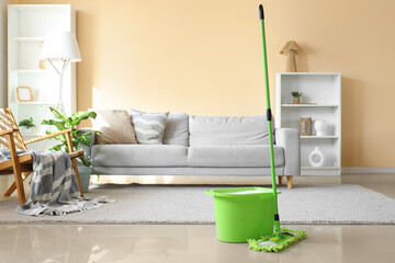 Mop with bucket on floor in living room interior
