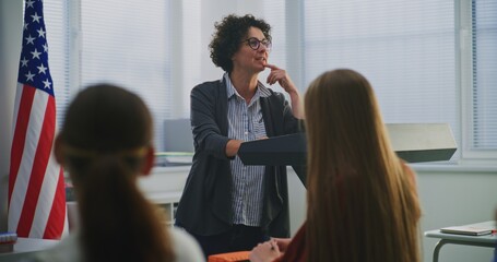 American Teacher Stands Podium Beside US Flag, Engaging Students In Open Discussion About National...
