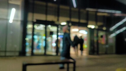 A woman walks along an evening street decorated for Christmas. Blurred. Along the storefronts of trendy shops and a cinema along evening street in blurred focus. Before Christmas