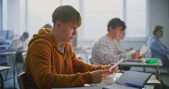 Two Teenagers Sit at Desks in Bright, Modern Classroom, Leaning Together Examine and Discuss Assignment Results. Concept Peer Collaboration, Sharing of Learning Experiences in Modern School Setting.