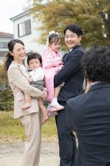 屋外で七五三や記念日のファミリーフォト　カメラ目線の笑顔の4人家族　カメラマンと一緒