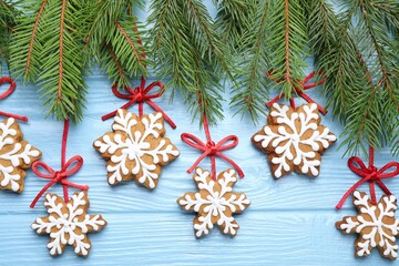 Tasty gingerbread cookies and fir tree branches on light blue wooden background, flat lay. Christmas treat