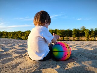 Small child and colorful ball on the beach on the sand. Rear view. Family spends time outdoors