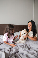 A woman and a child are sitting on a bed with a white dog