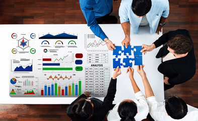 A diverse group of professionals engages in collaborative strategy development. They analyze charts and graphs while working together on puzzle pieces, symbolizing teamwork and innovation. Trope