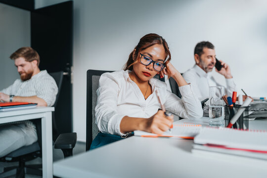 A diverse team in an open-plan office, concentrating on tasks, notes, and phone calls.