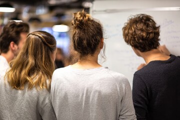 Startup brainstorming session in coworking space, team leaning over whiteboard, photographed from behind shoulders